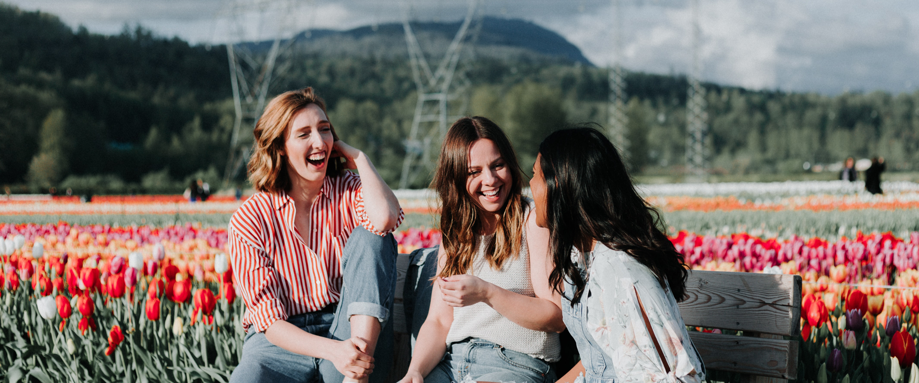 Three diverse women sitting on a bench in a field of tulips.